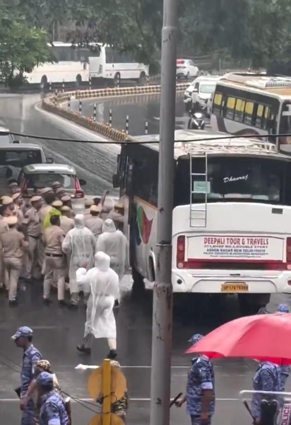 Police crowd around a detainee bus in heavy rain
